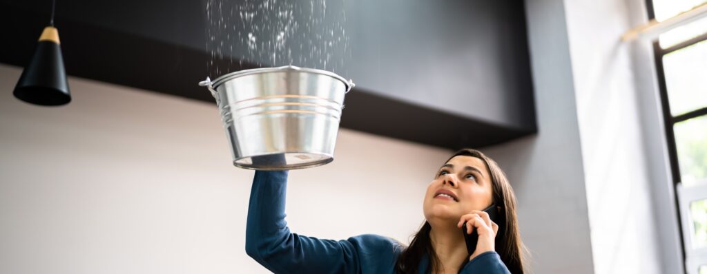 Homeowner holding bucket under leak calling emergency plumber